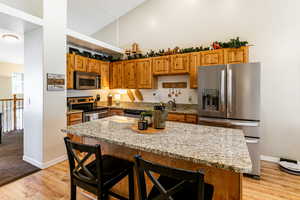 Kitchen featuring appliances with stainless steel finishes, a breakfast bar area, granite countertops, a kitchen island, and laminate wood-style flooring