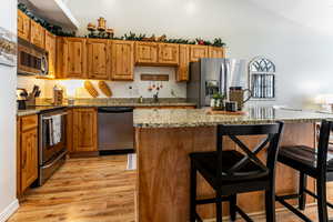 Kitchen with stainless steel appliances, a kitchen bar, granite countertops, an island with sink, and high vaulted ceiling