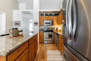 Kitchen with appliances with stainless steel finishes, laminate wood-type flooring, granite countertops, and cabinets