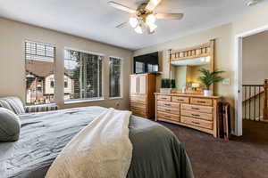 Primary bedroom featuring dark colored carpet and ceiling fan