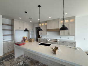 Kitchen featuring a kitchen bar, light stone counters, a center island with sink, glass insert cabinets, and recessed lighting