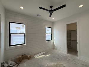 Unfurnished bedroom featuring wooden walls, a spacious closet, a ceiling fan, and recessed lighting