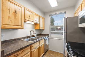 Kitchen featuring dark countertops, light brown cabinets, appliances with stainless steel finishes, and light tile patterned floors