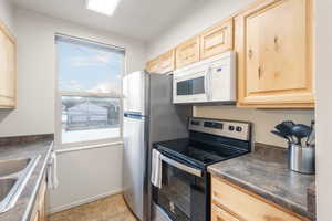 Kitchen featuring stainless steel electric range, dark countertops, light brown cabinets, and white microwave