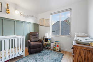Bedroom featuring a crib, light wood finished floors, and a decorative wall
