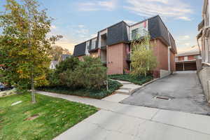 View of side of home featuring a shingled roof, mansard roof, brick siding, and a lawn