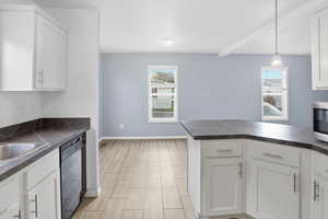 Kitchen featuring dark countertops, white cabinets, dishwasher, and beam ceiling