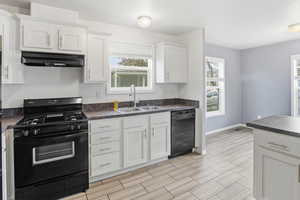 Kitchen featuring black appliances, dark countertops, white cabinets, range hood, and wood finish floors