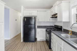 Kitchen with black appliances, white cabinets, under cabinet range hood, and wood tiled floors