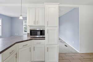 Kitchen with white cabinets, stainless steel microwave, pendant lighting, light carpet, and wood finish floors