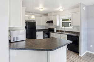 Kitchen featuring a peninsula, dark countertops, black appliances, white cabinets, and hanging light fixtures