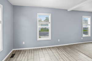 Empty room with plenty of natural light, beamed ceiling, and wood tiled floors