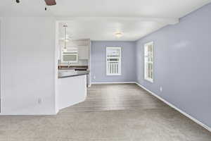 Unfurnished living room featuring light colored carpet, ceiling fan, wood tiled floors, and beamed ceiling