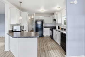 Kitchen with a peninsula, white cabinetry, black appliances, decorative light fixtures, and dark countertops