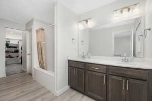 Bathroom with shower / bath combo with shower curtain, double vanity, light wood-style floors, and a walk in closet