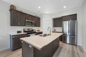 Kitchen featuring dark brown cabinetry, stainless steel appliances, light wood-style flooring, a center island with sink, and recessed lighting