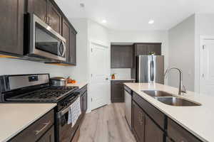 Kitchen with appliances with stainless steel finishes, dark brown cabinetry, light wood-type flooring, light stone counters, and recessed lighting