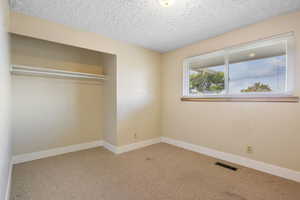 Unfurnished bedroom featuring carpet flooring, a textured ceiling, and a closet