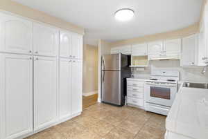Kitchen with tile countertops, white electric stove, white cabinets, freestanding refrigerator, and decorative backsplash