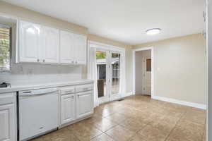Kitchen featuring tile countertops, white dishwasher, white cabinetry, and backsplash