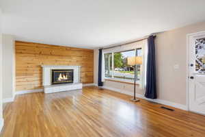 Unfurnished living room with wooden walls, light wood-type flooring, and a brick fireplace