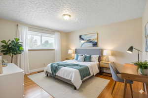 Digitally staged. Bedroom with wood finished floors and a textured ceiling