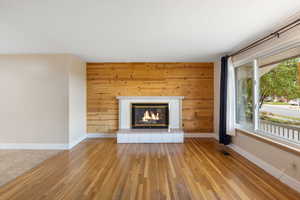 Unfurnished living room featuring wooden walls, wood finished floors, and a brick fireplace