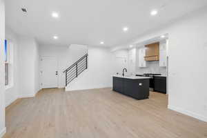 Kitchen with dark cabinetry, an island with sink, stainless steel range, light wood-style floors, and recessed lighting