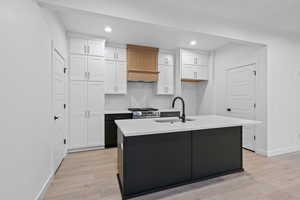 Kitchen with white cabinetry, dark cabinets, recessed lighting, light wood finished floors, and a center island with sink