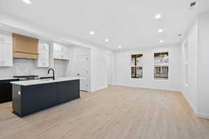 Kitchen featuring white cabinetry, recessed lighting, a kitchen island with sink, light wood-style flooring, and premium range hood