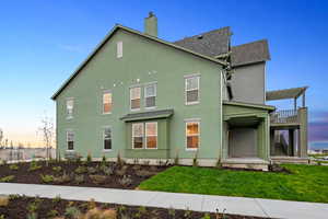 View of side of property featuring stucco siding, roof with shingles, stairs, a chimney, and a yard