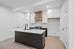 Kitchen with white cabinetry, light wood-style floors, a kitchen island with sink, recessed lighting, and light stone counters