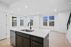 Kitchen with recessed lighting, light wood-style flooring, dishwasher, light stone countertops, and a center island with sink