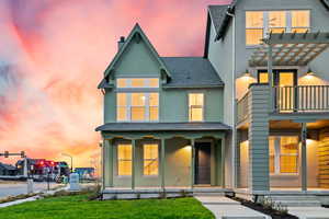 Back of property at dusk with roof with shingles, stucco siding, a porch, and a yard