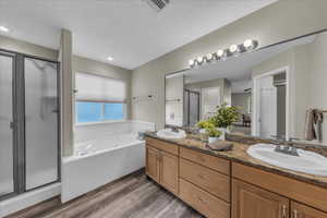 Bathroom featuring double vanity, a stall shower, light wood finished floors, a tub with jets, and a textured ceiling