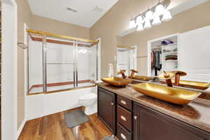 Full bath with bath / shower combo with glass door, a spacious closet, light wood-style flooring, and double vanity