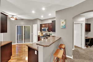 Kitchen featuring arched walkways, decorative backsplash, a breakfast bar area, stainless steel appliances, and dark brown cabinets