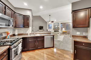 Kitchen with stainless steel appliances, lofted ceiling, a ceiling fan, light wood-style floors, and a fireplace