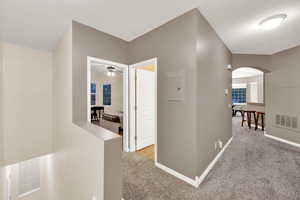 Corridor featuring light colored carpet, arched walkways, and an upstairs landing