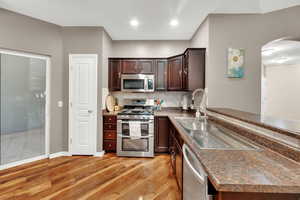 Kitchen featuring stainless steel appliances, dark countertops, decorative backsplash, arched walkways, and light wood-style floors