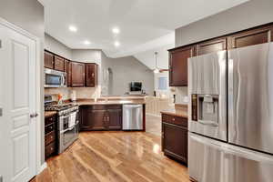 Kitchen featuring stainless steel appliances, decorative backsplash, open floor plan, dark brown cabinetry, and ceiling fan