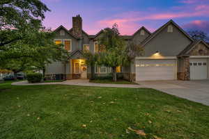 View of front of house with stone siding, stucco siding, driveway, a yard, and a garage