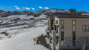 View of snow covered exterior with stone siding, a mountain view, and a chimney