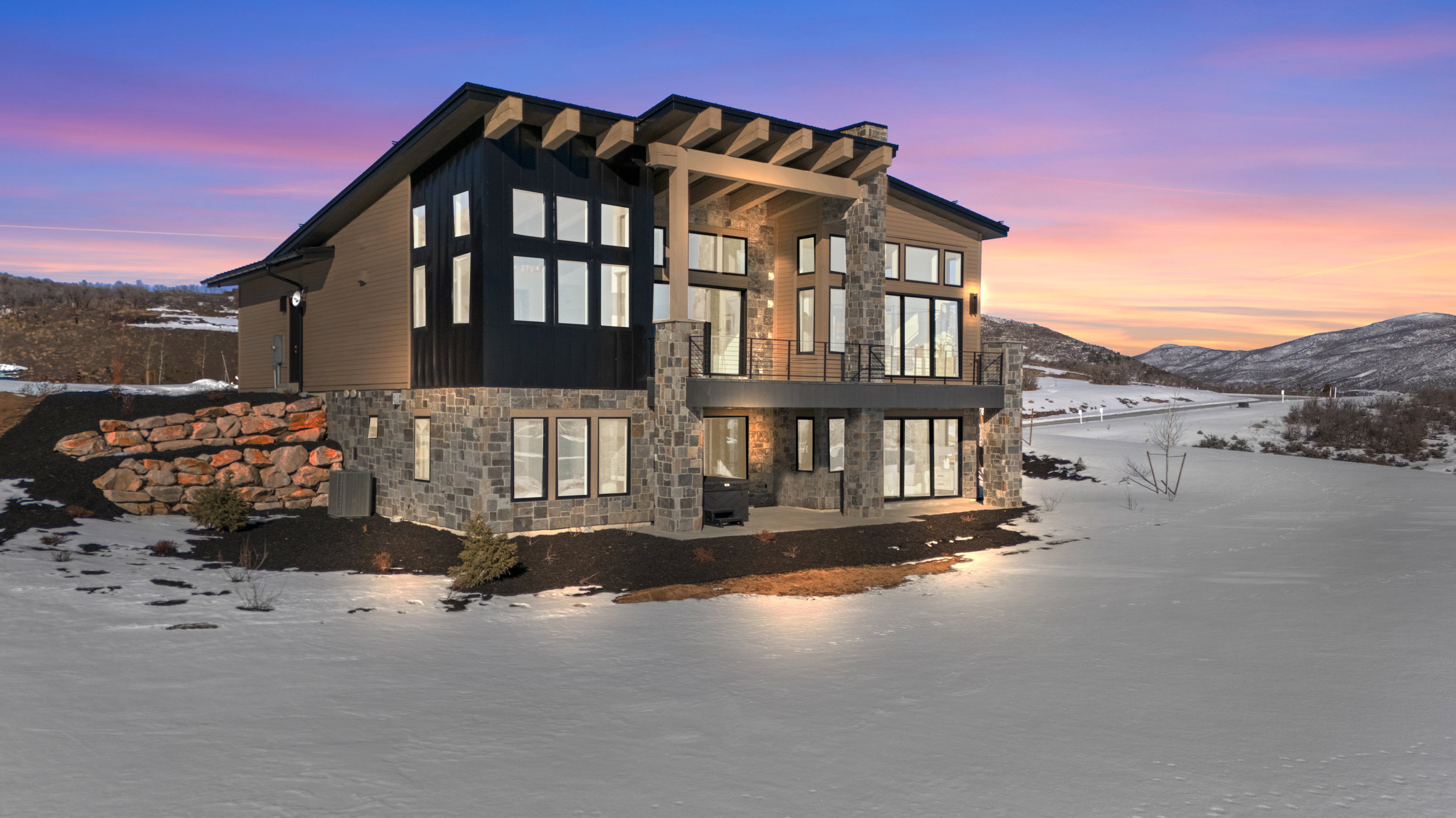 Snow covered rear of property featuring stone siding, a mountain view, and a balcony
