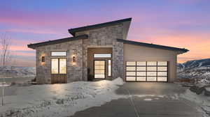 Contemporary home featuring an attached garage, stone siding, concrete driveway, and a mountain view