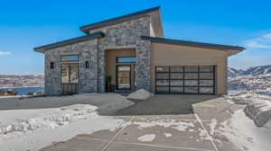 Modern home with an attached garage, stone siding, a water and mountain view, and concrete driveway