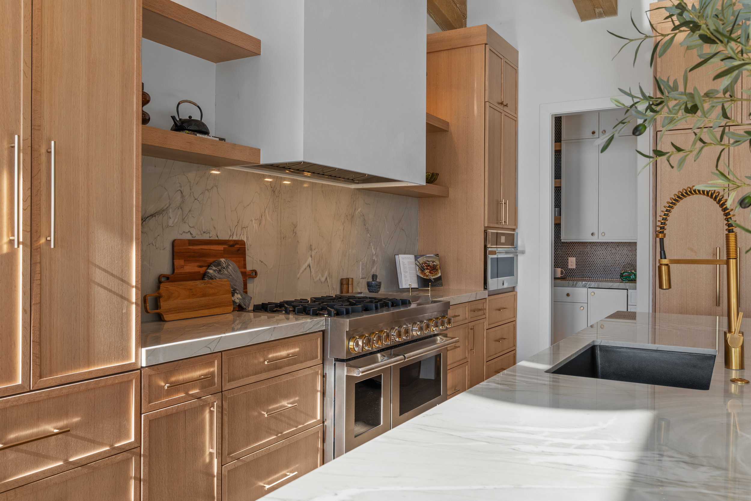 Kitchen with decorative backsplash, appliances with stainless steel finishes, wall chimney exhaust hood, open shelves, and brown cabinetry