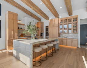Kitchen with open shelves, a kitchen breakfast bar, light stone counters, glass insert cabinets, and beamed ceiling