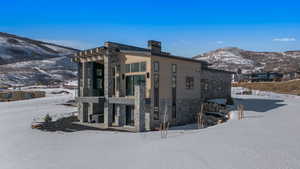View of snowy exterior with a balcony, stone siding, a mountain view, a chimney, and a patio