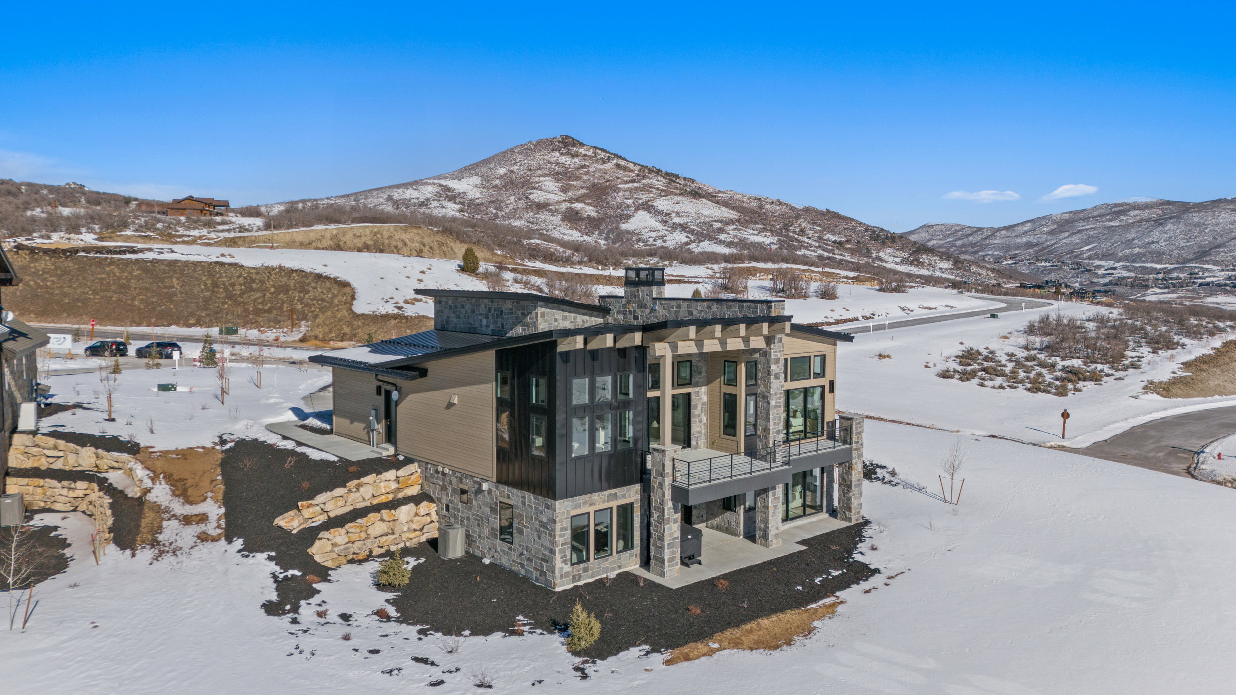 Snow covered property featuring stone siding, a chimney, a balcony, a patio, and a mountain view